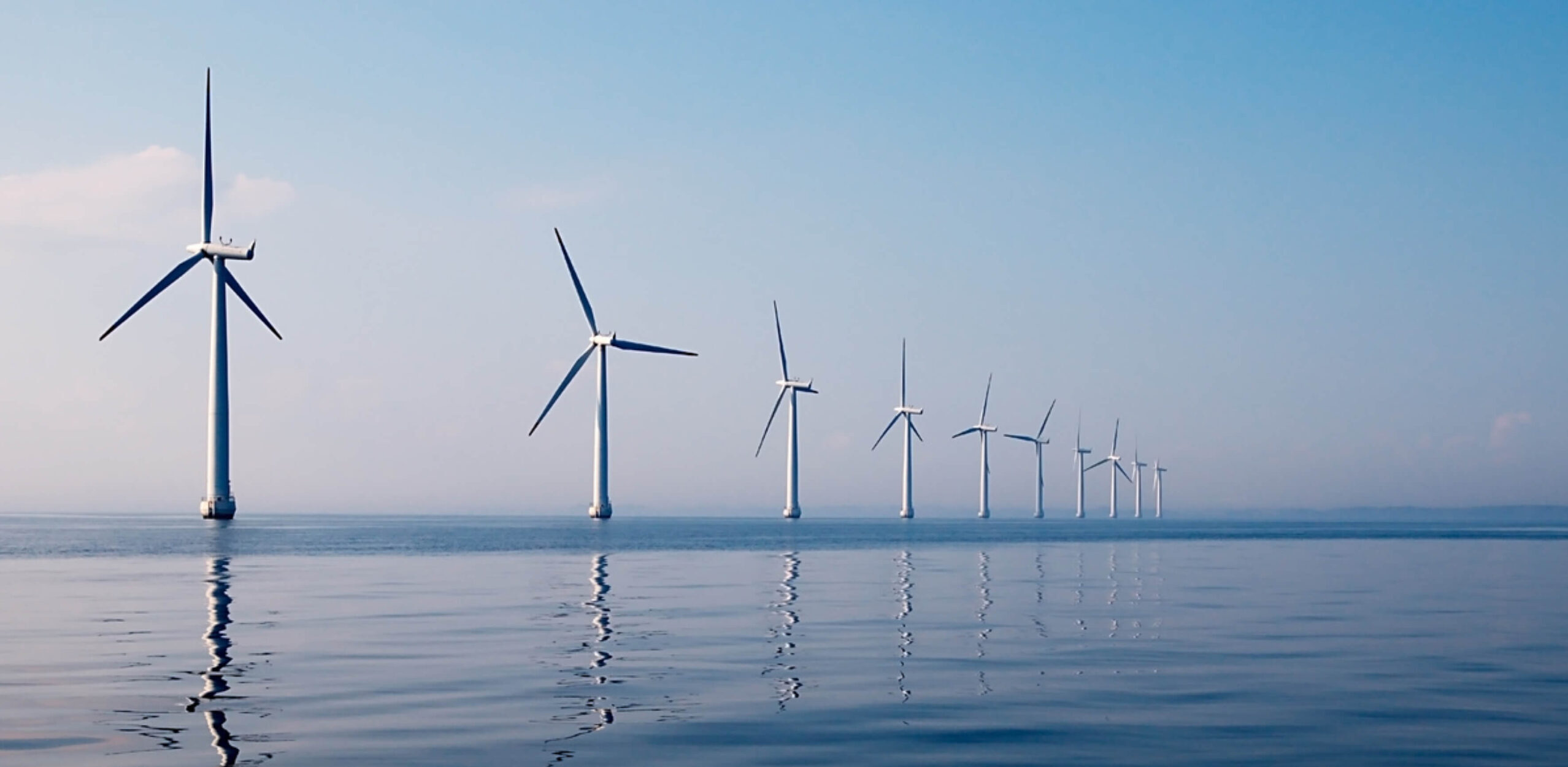 Reihe von Windkraftanlagen im Meer bei klarem Himmel – Symbol für nachhaltige Energiegewinnung und langfristige Umweltverantwortung.