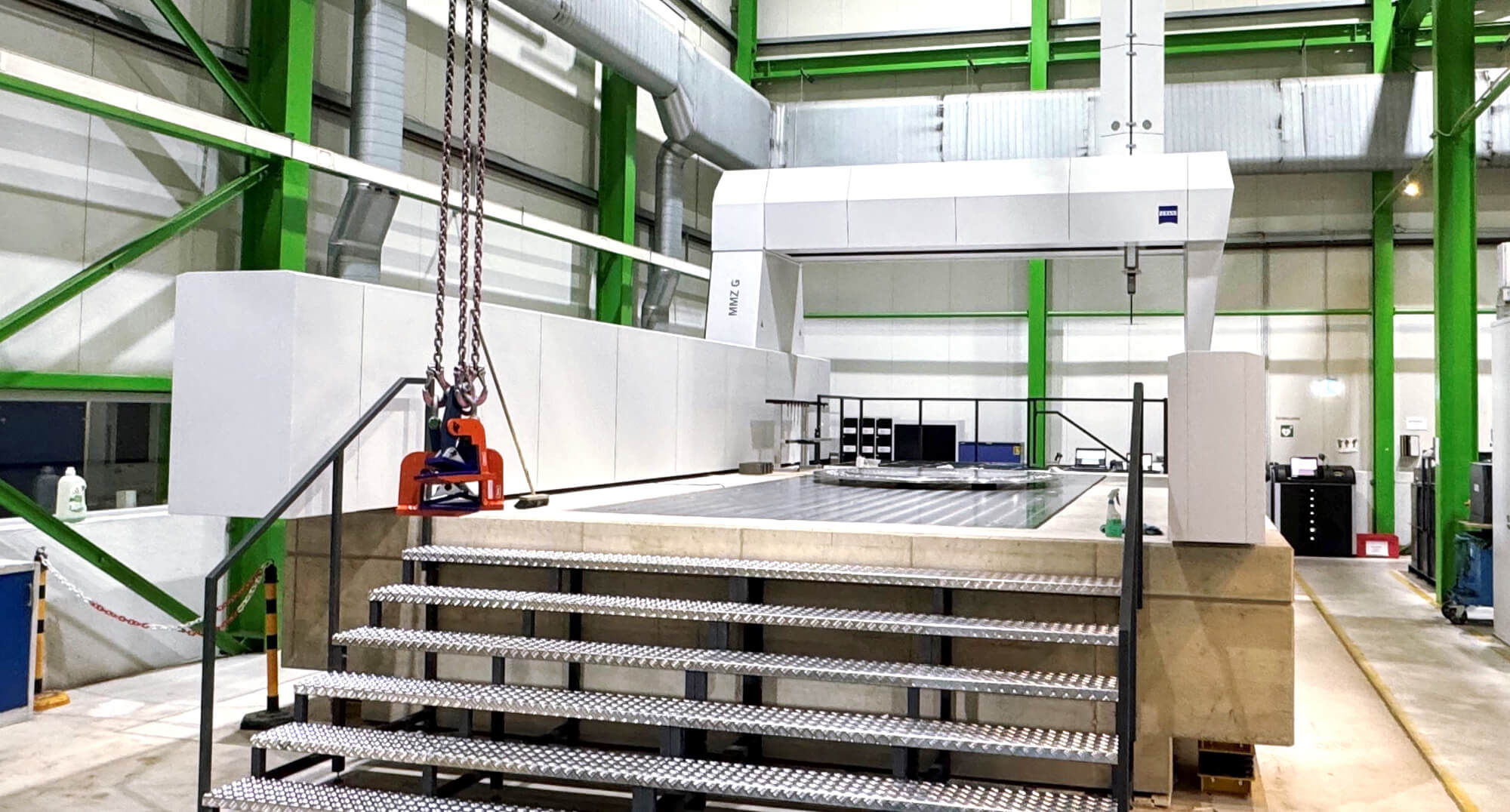 Koordinatenmessmaschine in der Produktionshalle von HSP Components, umgeben von grüner Stahlkonstruktion und Treppenaufgang zur Messplattform.