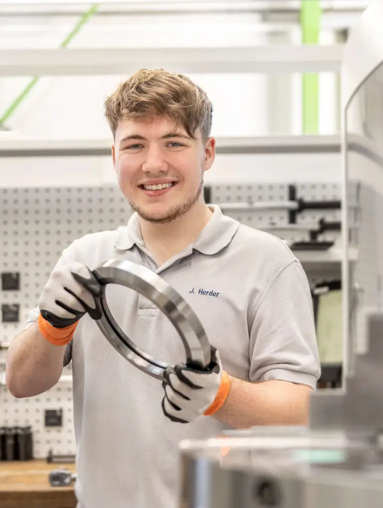 Ein HSP Auszubildender hält ein Präzisionsdrehteil nach der Entnahme aus der Maschine in beiden Händen.