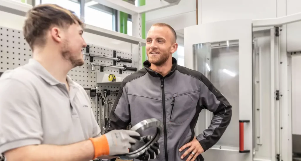 Ein HSP Auszubildender und ein Ausbilder besprechen die Qualität eines Werkstücks in der Fertigung.